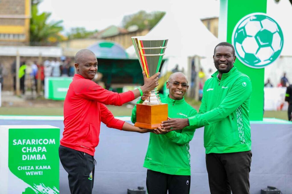 Safaricom CEO Peter Ndegwa (centre), Nairobi Senator Edwin Sifuna and Football Kenya Federation President Nick Mwendwa display Safaricom Chapa Dimba na Safaricom Season Four Trophy at Camp Toyoyo grounds in Nairobi.