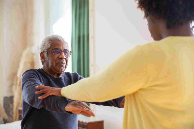 Older African man receiving supportive care from a caregiver during rehabilitation therapy.