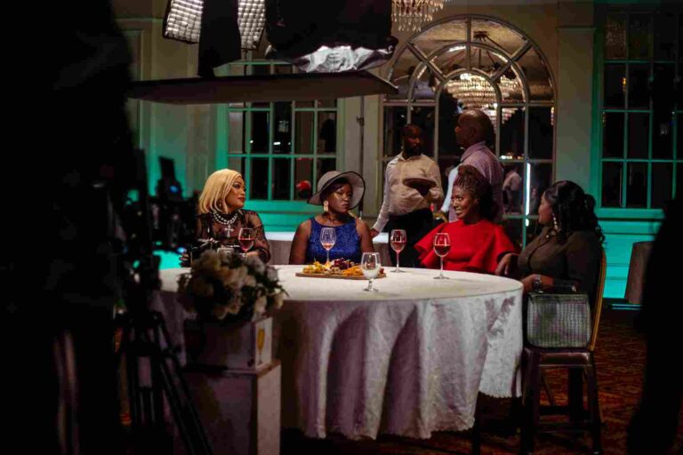 Single Kiasi cast filming a dinner scene with wine and formal wear, under studio lighting. Image Description: A behind-the-scenes look at a formal dinner scene from Single Kiasi Season 4. Five cast members are seated around a table with wine and plated meals, while crew members and lighting equipment are visible in the background. The elegant setting and cinematic setup suggest a pivotal moment in the storyline, possibly involving relationship dynamics or dramatic revelations. Would you like me to tailor these for Instagram alt captions or LinkedIn accessibility tags as well? I can also suggest image filenames and metadata keywords to boost search visibility.