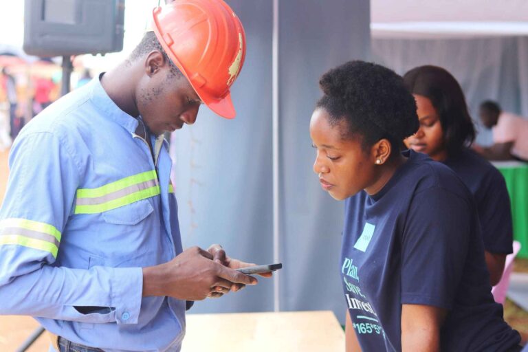 - XENO representative reviewing mobile app with field worker - Title: On-Site Engagement with XENO Investment App - Caption: A XENO team member demonstrates the investment app to a field worker during an outreach event, showcasing mobile-first financial planning. - Description: The image shows a construction worker in safety gear interacting with a XENO representative. They are reviewing something on a smartphone, likely the XENO app. This moment illustrates XENO’s commitment to reaching underserved populations with accessible, tech-enabled financial solutions.