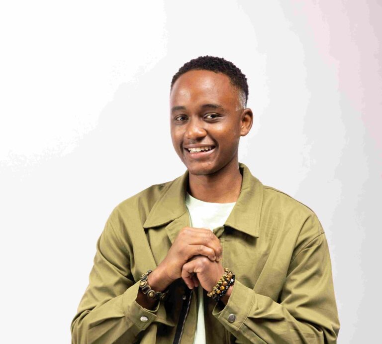 Meet Isaac Okoyo: The Breakout Star of Reuben Odanga’s Lazizi Okoyo Isaac stands smiling in a studio portrait, wearing layered green tones and beaded bracelets, hands clasped in front of his chest.