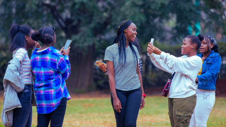 Young Kenyans socializing outdoors, taking photos and enjoying a casual moment together.