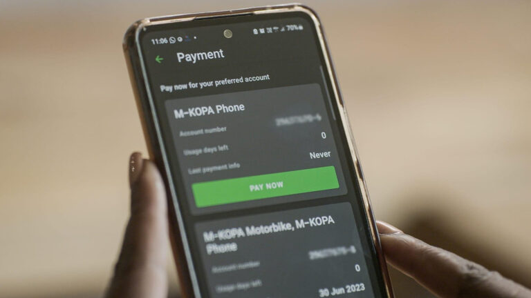 Hand holding phone showing M-KOPA payment screen for financed device