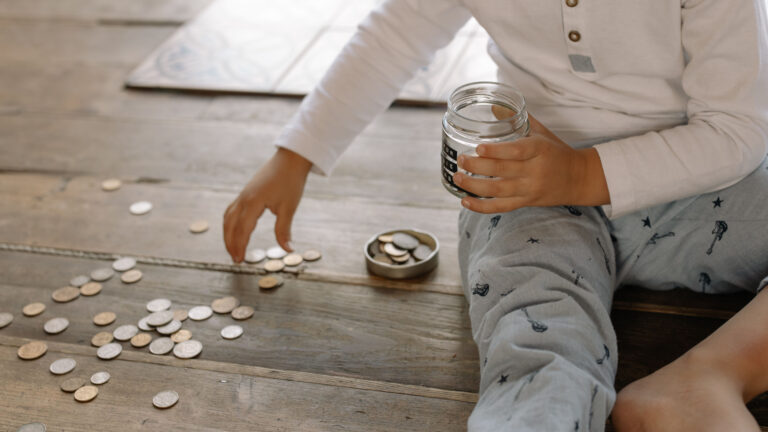 Young child dropping coins into a savings jar on a wooden floor, symbolizing early investing for kids in Kenya