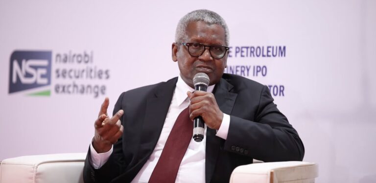 Aliko Dangote speaking into a microphone at a Nairobi Securities Exchange investor event, with an NSE logo and Dangote Petroleum Refinery IPO signage behind him.