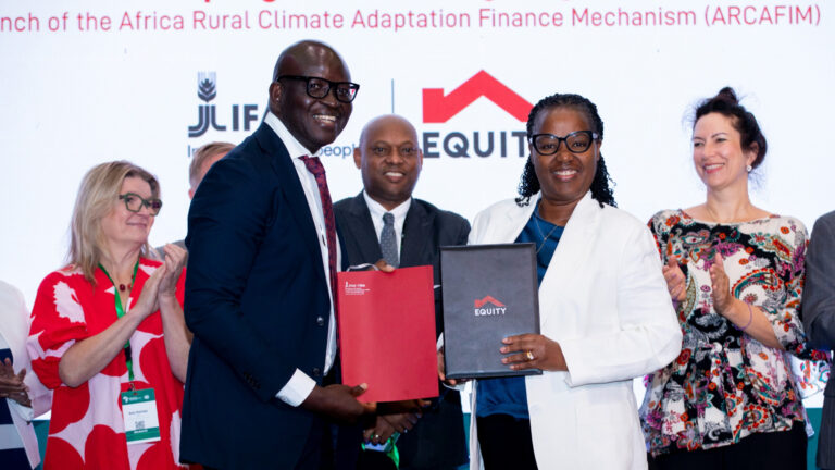 IFAD and Equity Group representatives shake hands while holding signed folders at the ARCAFIM partnership signing ceremony, with delegates applauding in the background.