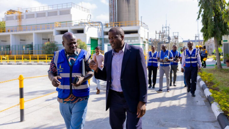 KPLC and Bamburi Cement officials walking through the Mombasa Plant grounds during a site visit, with plant infrastructure and a power substation in the background.