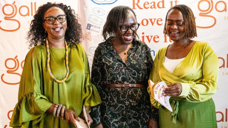 Three women stand in front of Galleria Shopping Mall and Passportz & Pagez banners at a book club event. Two hold books, and one holds a copy of Who Moved My Cheese?