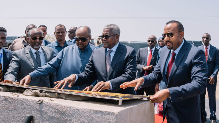 Ethiopian Prime Minister Abiy Ahmed, Djibouti President Ismail Omar Guelleh and Nigerian billionaire Aliko Dangote touching a commemorative plaque set into a concrete cornerstone during an outdoor groundbreaking ceremony.