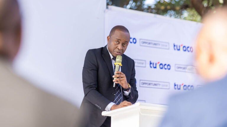 Cedrick Todwell speaks into a microphone at a podium in front of a Turaco and Opportunity Bank backdrop.