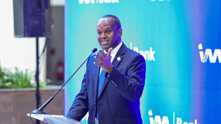 Man in a suit and tie speaks at a podium with a microphone, in front of an I&M Bank backdrop.