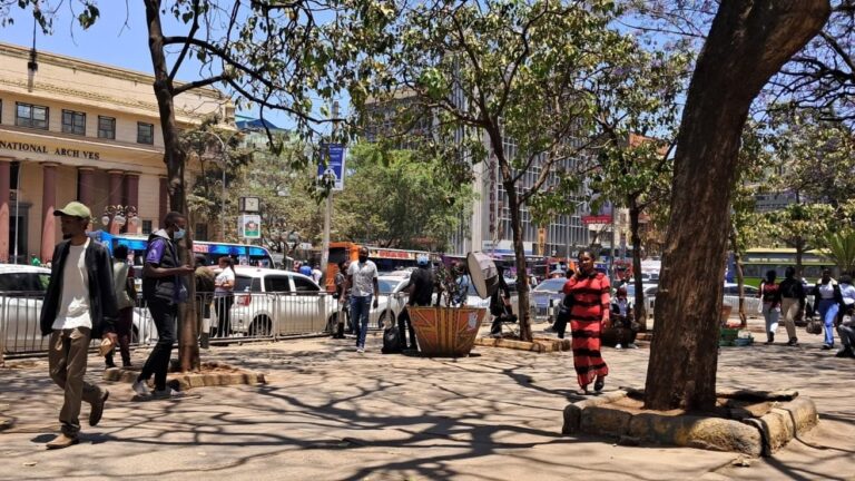Pedestrians walk past street vendors and parked cars outside the Kenya National Archives in Nairobi.