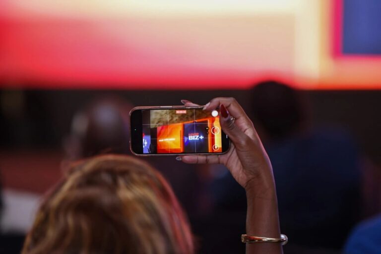 An attendee at the LOOP BIZ+ launch holds up a phone and records the LOOP BIZ+ logo on the event screen.