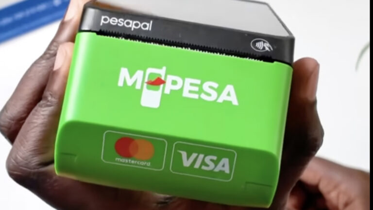 A hand holds a Pesapal point of sale terminal with a green M-PESA casing. The NFC contactless symbol sits on the top edge, and Mastercard and Visa logos appear on the front.